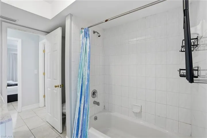 Bathroom featuring shower / bath combo with shower curtain, light tile patterned floors, and connected bathroom