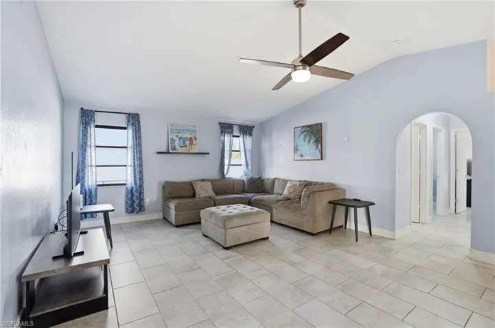 Living room with arched walkways, vaulted ceiling, ceiling fan, and light tile patterned floors