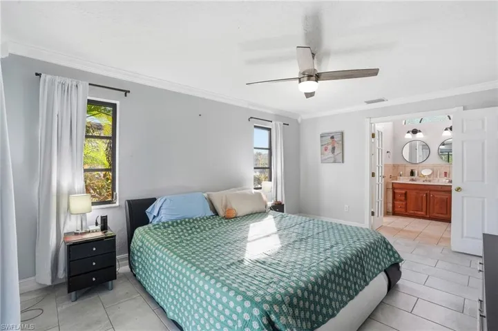 Bedroom featuring crown molding, ceiling fan, light tile patterned flooring, and ensuite bath