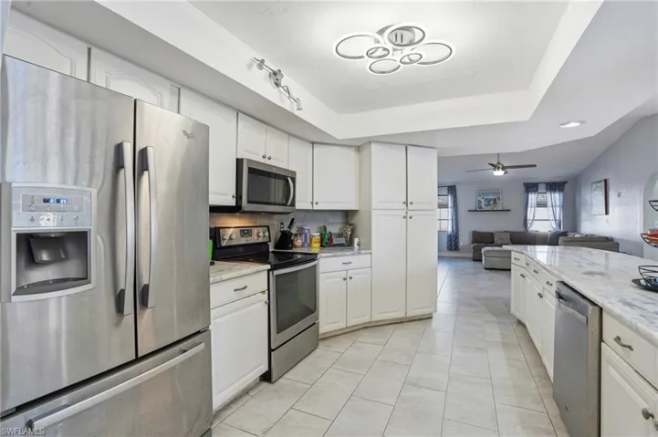 Kitchen featuring appliances with stainless steel finishes, open floor plan, white cabinetry, and light stone counters