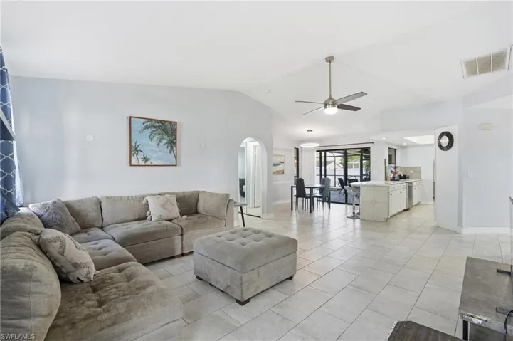 Living area with a ceiling fan, lofted ceiling, light tile patterned floors, and arched walkways