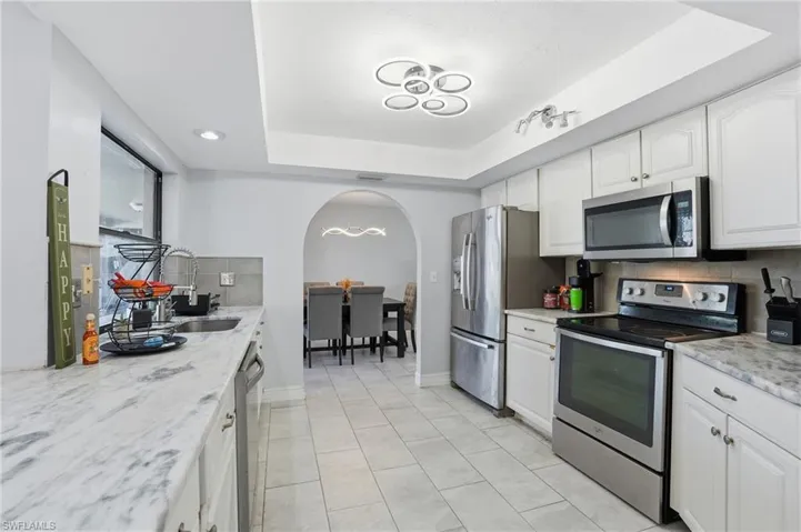 Kitchen featuring tasteful backsplash, appliances with stainless steel finishes, a tray ceiling, and white cabinetry