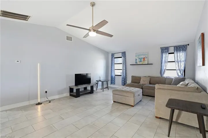 Living area with lofted ceiling, ceiling fan, and light tile patterned flooring