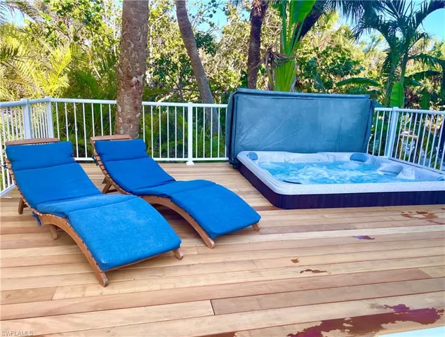 Expansive wood-finish deck featuring a built-in hot tub, white railing, and lush tropical landscaping