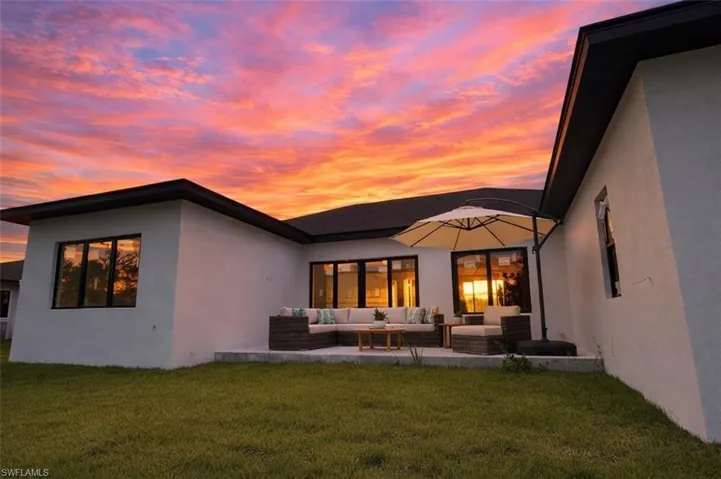Back of property at dusk with a lawn, stucco siding, a patio area, and an outdoor hangout area
