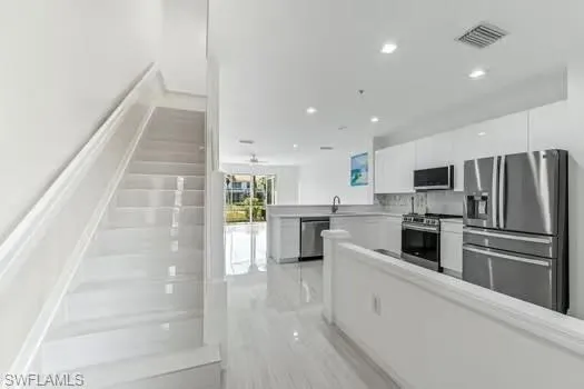 Kitchen with appliances with stainless steel finishes, white cabinetry, recessed lighting, a peninsula, and light countertops