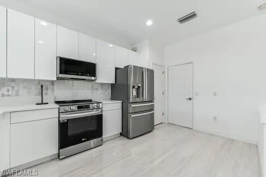 Kitchen featuring appliances with stainless steel finishes, white cabinets, light countertops, backsplash, and light wood-style flooring