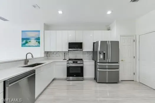 Kitchen featuring stainless steel appliances, white cabinetry, modern cabinets, and light countertops