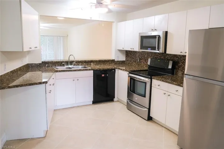 Kitchen featuring appliances with stainless steel finishes, white cabinets, ceiling fan, sink, and dark stone counters