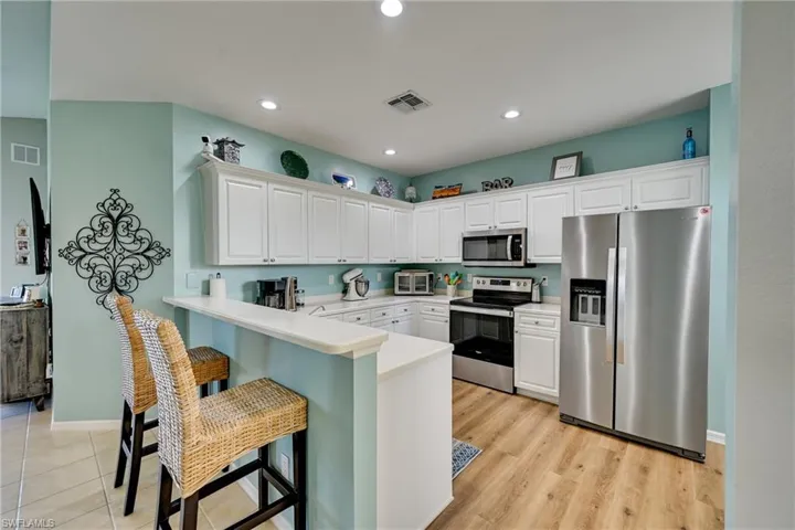 Kitchen featuring white cabinetry, wood-finish flooring, stainless steel appliances, and a breakfast bar with a solid surface countertop
