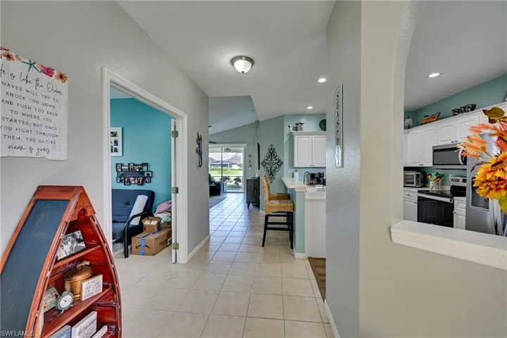 Ceramic tile flooring, arched wall pass-through, and kitchen featuring white cabinetry and stainless-steel appliances