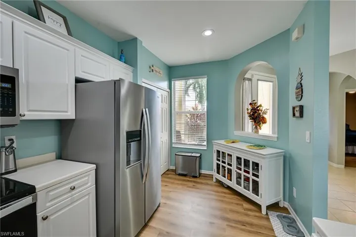 Kitchen featuring white cabinetry, stainless steel refrigerator, wood-finish flooring, recessed lighting, and a decorative arched wall niche