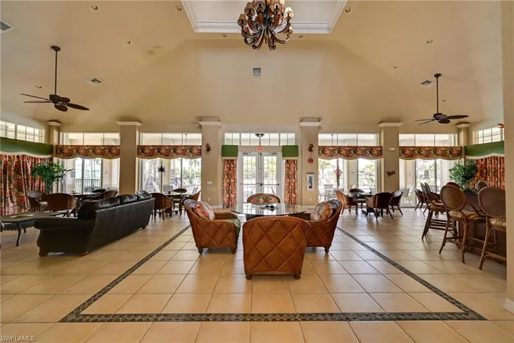 Spacious common area featuring vaulted ceilings with recessed lighting, central tray ceiling with a decorative chandelier, tile flooring with geometric border inlay, and floor-to-ceiling windows