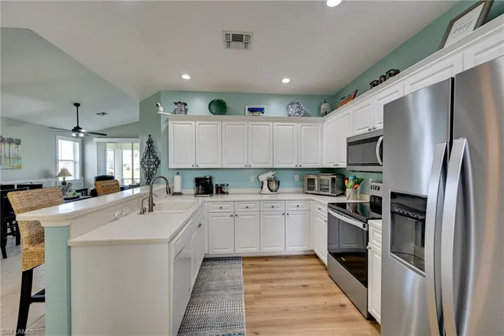 Kitchen featuring white cabinetry, wood-finish flooring, stainless steel appliances, and a breakfast bar with a solid surface countertop