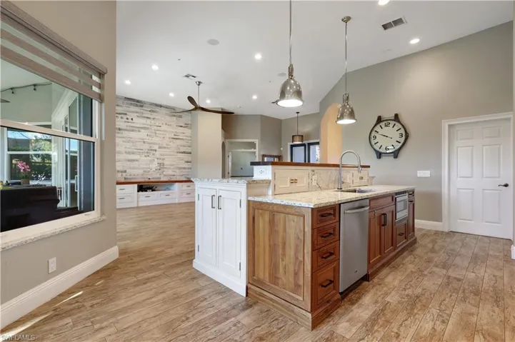 Kitchen with light stone countertops, a kitchen island with sink, hanging light fixtures, light wood-style flooring, and recessed lighting