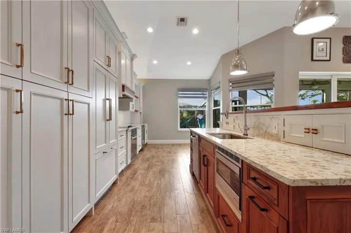 Kitchen featuring pendant lighting, vaulted ceiling, light stone counters, appliances with stainless steel finishes, and light wood-style floors