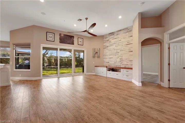 Unfurnished living room with arched walkways, light wood-type flooring, a ceiling fan, recessed lighting, and a towering ceiling