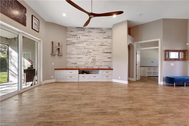 Unfurnished living room featuring arched walkways, a ceiling fan, light wood finished floors, an accent wall, and recessed lighting