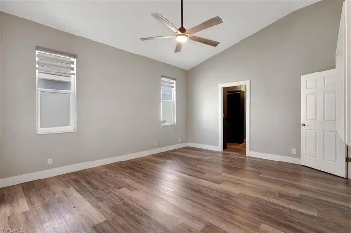 Unfurnished bedroom featuring a spacious closet, wood finished floors, a ceiling fan, and high vaulted ceiling