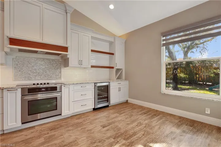 Kitchen featuring lofted ceiling, white cabinets, open shelves, light stone counters, and stainless steel oven