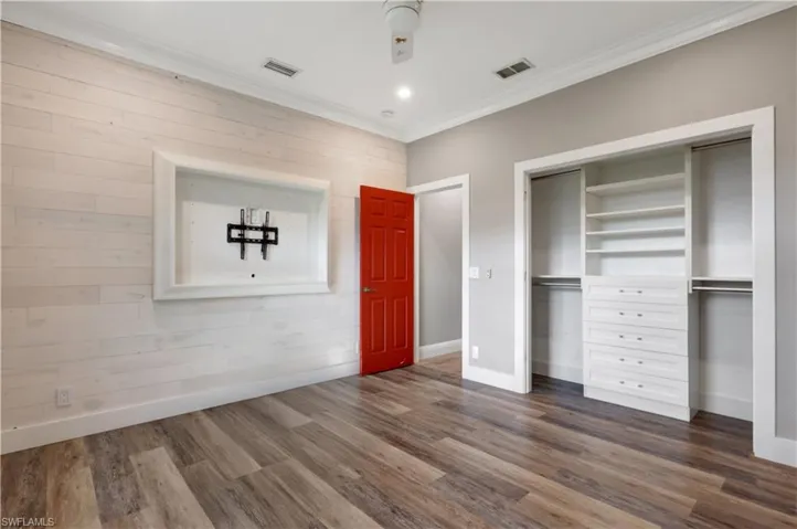 Unfurnished bedroom with a closet, dark wood-style floors, ornamental molding, an accent wall, and recessed lighting