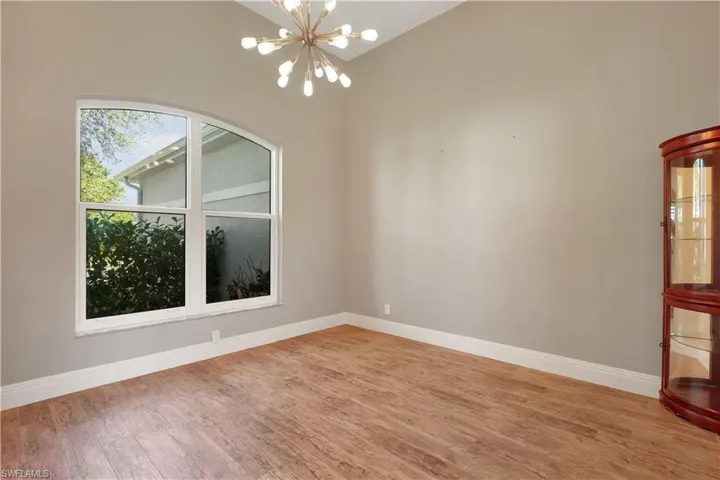 Empty room featuring a chandelier, light wood-type flooring, and lofted ceiling