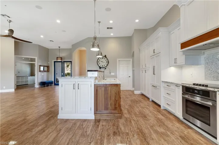 Kitchen with white cabinetry, arched walkways, oven, pendant lighting, and light stone counters