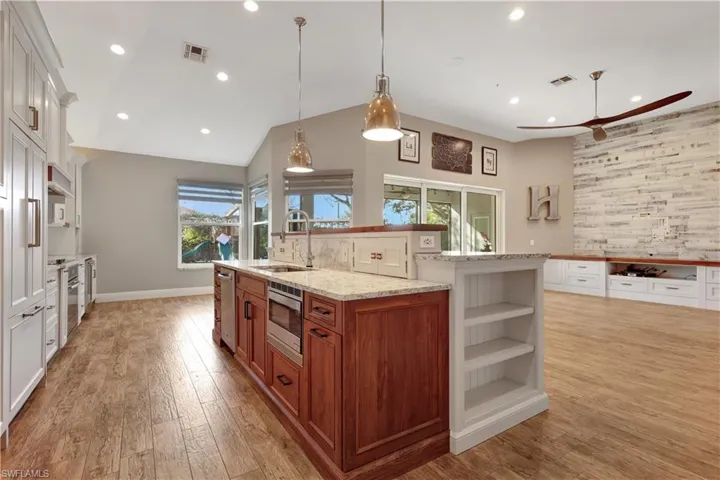 Kitchen with brown cabinets, pendant lighting, a kitchen island with sink, light stone counters, and light wood-type flooring