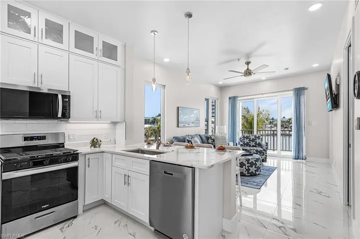 Open-concept living space with white kitchen cabinetry, stainless steel appliances, and a central island with a sink - Virtually Edited Image