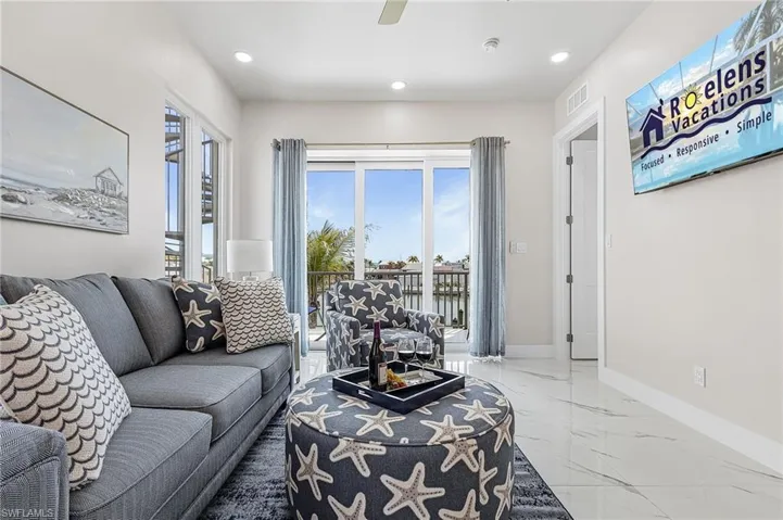 Bright living area featuring large sliding glass doors, recessed lighting, and tile flooring - Virtually Edited Image