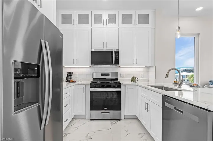 Contemporary kitchen featuring white cabinetry, stainless steel appliances, and white marble-look flooring - Virtually Edited Image