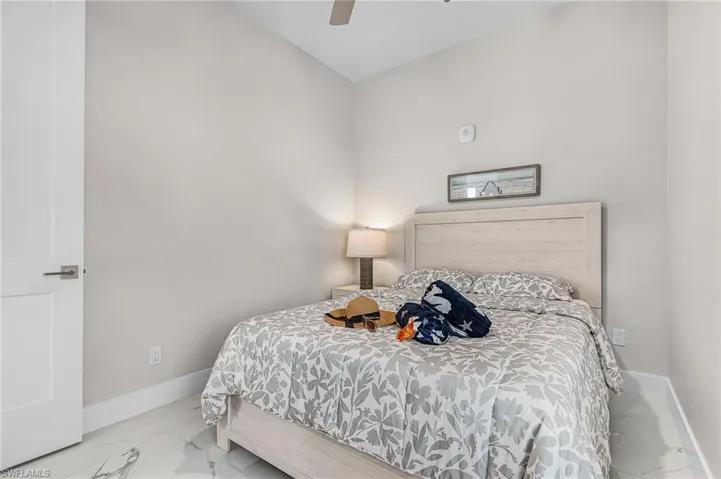 Spacious bedroom featuring light neutral wall tones, a modern ceiling fan, and white baseboards - Virtually Edited Image