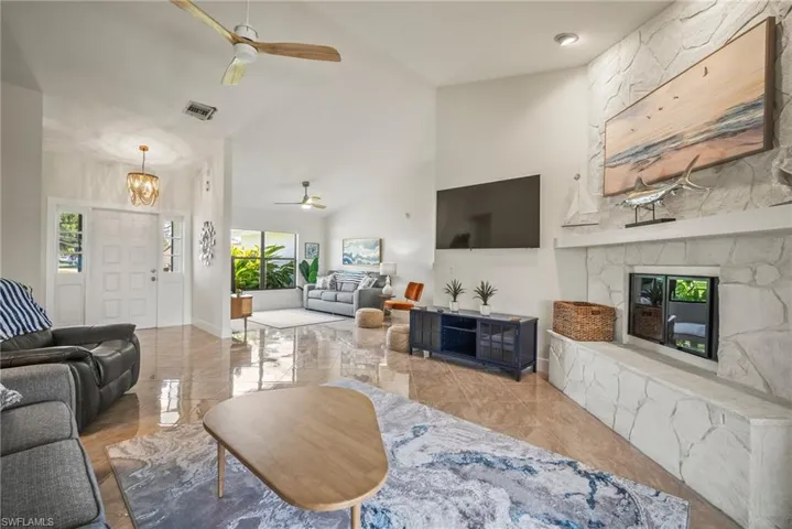 Living room with marble finish floor, visible vents, a fireplace, high vaulted ceiling, and ceiling fan with notable chandelier