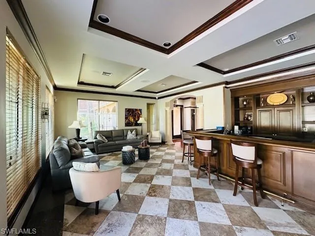 Living area featuring arched walkways, crown molding, a bar, and a tray ceiling