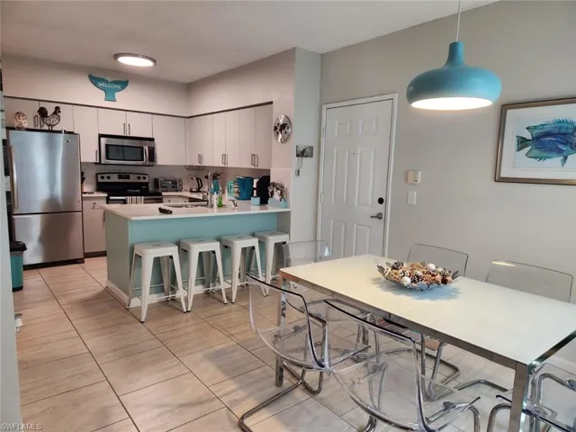 Kitchen featuring appliances with stainless steel finishes, light countertops, white cabinetry, a kitchen breakfast bar, and decorative light fixtures