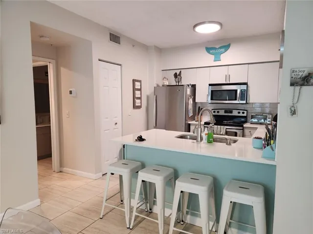Kitchen featuring a peninsula, white cabinets, a kitchen bar, stainless steel appliances, and backsplash
