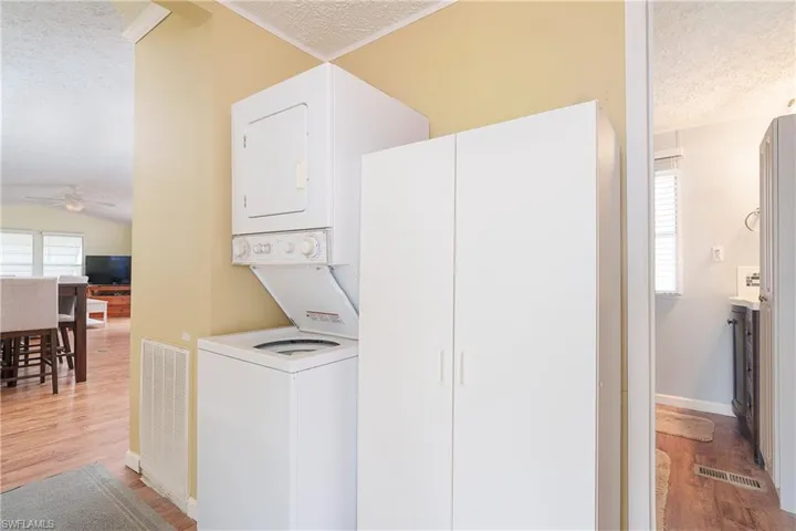 Laundry area with a textured ceiling, light wood-style flooring, stacked washing machine and dryer, and a ceiling fan