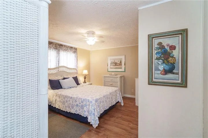 Bedroom featuring a textured ceiling, wood finished floors, ornamental molding, and a ceiling fan