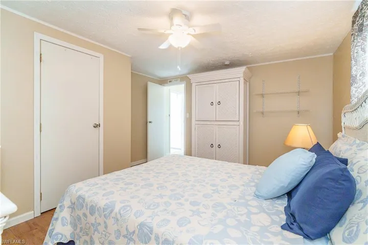 Bedroom with a textured ceiling, light wood-type flooring, crown molding, a ceiling fan, and a closet