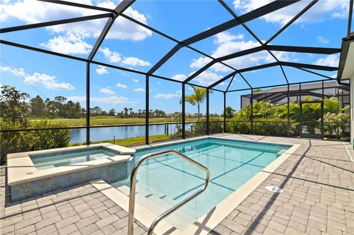 View of pool with a patio, glass enclosure, a pool with connected hot tub, and a water view
