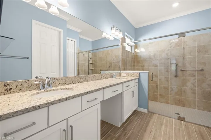 Bathroom with double vanity, a shower stall, wood tiled floors, and crown molding