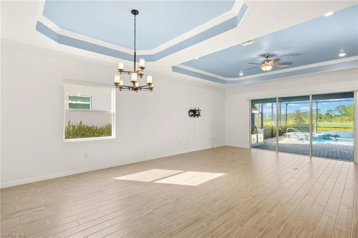 Spare room featuring a tray ceiling, crown molding, ceiling fan, a chandelier, and light wood-type flooring