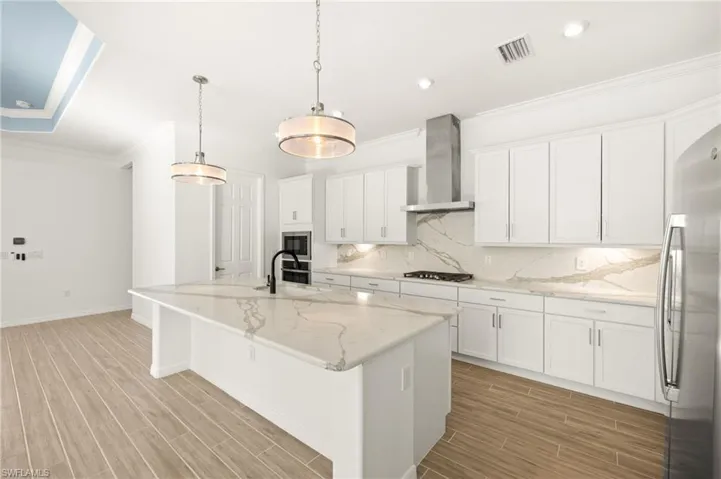 Kitchen with wall chimney exhaust hood, appliances with stainless steel finishes, ornamental molding, light wood-style flooring, and tasteful backsplash