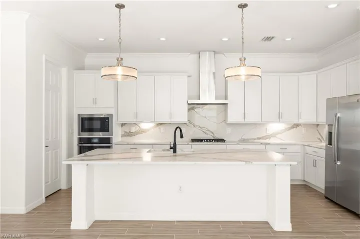Kitchen with stainless steel appliances, wall chimney range hood, wood tiled floors, an island with sink, and recessed lighting