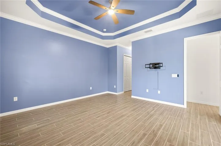 Empty room featuring a raised ceiling, ceiling fan, wood finished floors, and crown molding