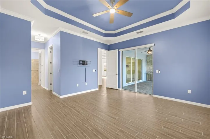 Unfurnished room featuring a ceiling fan, a tray ceiling, ornamental molding, and wood finished floors