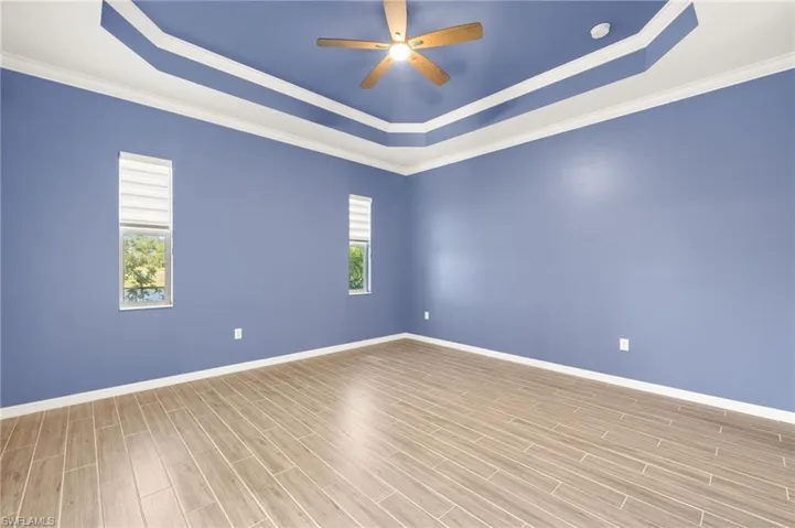 Empty room with a raised ceiling, crown molding, a ceiling fan, wood finished floors, and a smoke detector
