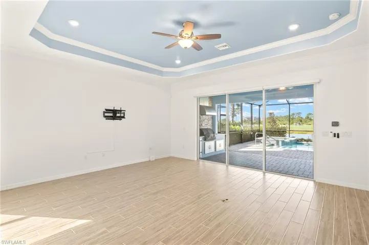 Spare room featuring a raised ceiling, ceiling fan, light wood finished floors, ornamental molding, and a smoke detector