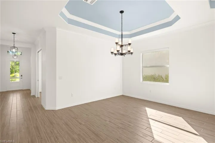 Unfurnished room featuring a chandelier, wood finished floors, crown molding, and a raised ceiling