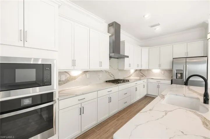 Kitchen featuring wall chimney exhaust hood, appliances with stainless steel finishes, crown molding, white cabinetry, and light wood finished floors